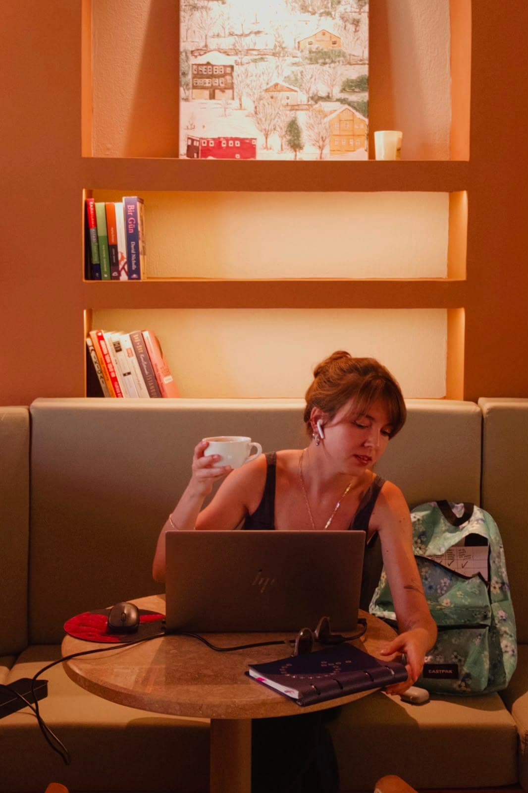 Banket koltukta laptopuyla çalışan bir misafir, arkasında kitap rafları
